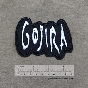 May include: Black and white embroidered patch with the word "GOJIRA" in a stylized font. The patch is approximately 3 inches wide.