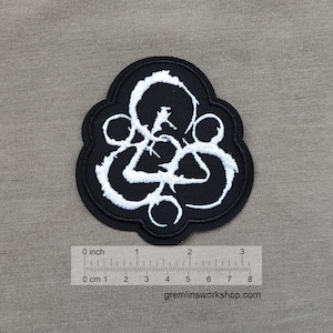 May include: Black and white embroidered patch with a unique design. The patch features a black background with a white abstract design. The patch is approximately 3 inches wide. The website gremlinsworkshop.com is printed at the bottom.