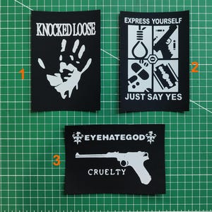 May include: Three black patches with white graphics and text. One patch reads "KNOCKED LOOSE" above a handprint. Another says "EXPRESS YOURSELF" and "JUST SAY YES" with images. The third patch says "EYEHATEGOD" and "CRUELTY" with a gun graphic.
