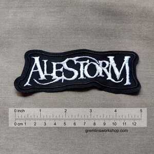 May include: Black and white embroidered patch with the band name "ALESTORM" in a stylized font.