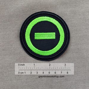 May include: Circular patch with a black background and a neon green design. The design features a neon green circle with a horizontal rectangle inside. The patch is approximately 3 inches in diameter. The text "gremlinsworkshop.com" is at the bottom.