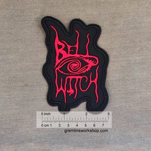 Op de afbeelding: Zwarte patch met rode geborduurde tekst en een oogontwerp. De tekst luidt "Bell Witch" in een gestileerd lettertype. De patch is ongeveer 7,6 cm breed.