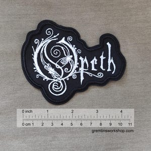 May include: Black and white embroidered patch with the word "Opeth" in a stylized font. The patch is approximately 3 inches wide.