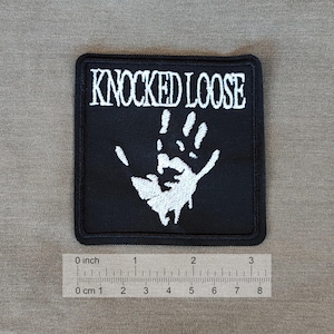 Puede incluir: Parche bordado negro con letras blancas que dicen "KNOCKED LOOSE" y una huella de mano blanca. El parche mide aproximadamente 5 cm de ancho.