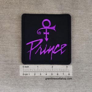 May include: A square black patch featuring the word "Prince" in a stylized purple font, along with a purple symbol. The patch measures approximately 3 inches wide. The design is embroidered.