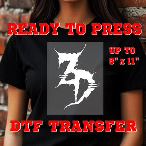 May include: Black t-shirt featuring a white, stylized "Z" graphic. The design has sharp, angular lines. Red text reads "READY TO PRESS" and "DTF TRANSFER". The image also includes the text "UP TO 20.3cm x 28cm".