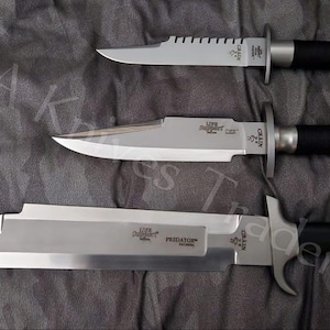 May include: Three fixed-blade knives with silver-toned steel blades and black handles. The top two knives feature serrated spines, while the largest bottom knife is labeled Predator. Each blade includes a metal guard and a black grip handle.