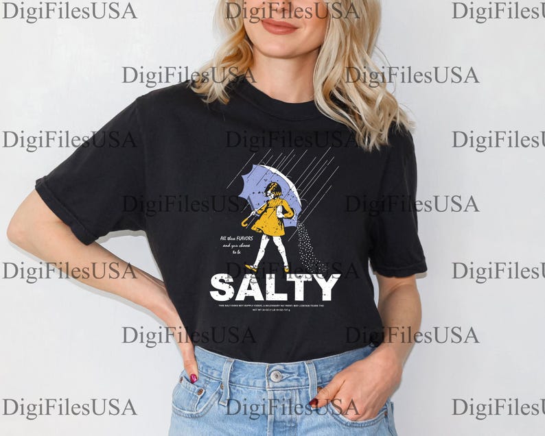 May include: Black t-shirt featuring a graphic of a person under an umbrella, with the word "SALTY" in bold white letters. The person is wearing a yellow dress and holding a blue umbrella. The shirt has the text "All the flavors and you choose to be".