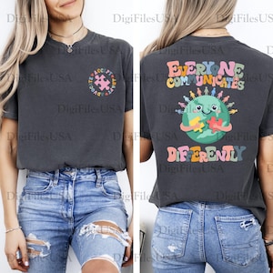 May include: Dark gray t-shirt with a colorful graphic on the front and back. The front features a puzzle piece design with the words "Accept, Advocate" and the back says "Everyone Communicates Differently" with a globe and puzzle pieces.