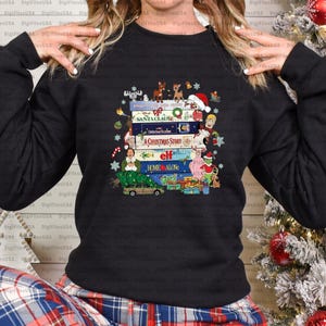Puede incluir: Sudadera negra con un diseño de películas navideñas, incluyendo "Santa Clause", "A Christmas Story", "Elf" y "Home Alone". El diseño incluye personajes de dibujos animados y elementos festivos.