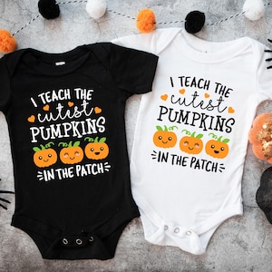 Könnte beinhalten: Zwei Baby-Bodys, einer schwarz und einer weiß, mit dem Text "I teach the cutest pumpkins in the patch". Das Design umfasst orangefarbene Kürbisse und Herzen, perfekt für Halloween oder den Herbst.