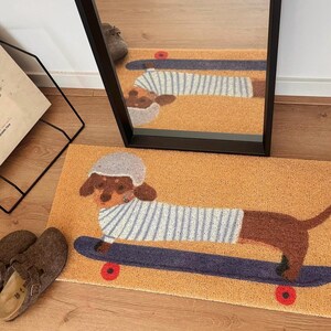 May include: A doormat featuring a brown dachshund wearing a striped shirt and a gray helmet, skateboarding on a blue board with red wheels. The mat has a tan background and is reflected in a nearby mirror.