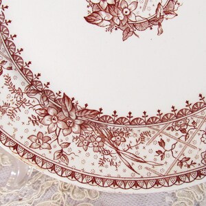 Pu&ograve; includere: Un piatto bianco con un motivo floreale marrone dettagliato. Il design include fiori, foglie e forme geometriche sul bordo. Il piatto ha un'estetica vintage.