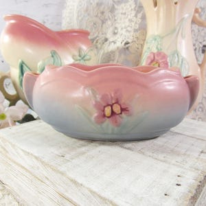 May include: An oval ceramic bowl featuring a scalloped rim and a gradient finish transitioning from soft pink at the top to a muted blue at the base. The center of the bowl is decorated with a raised, molded pink flower with green leaves.