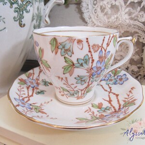 May include: A vintage teacup and saucer set with a floral pattern in shades of blue, green, and brown. The cup and saucer have a gold trim.