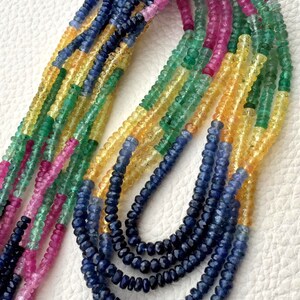 Può includere: Una collezione di collane di pietre preziose in vari colori. I fili presentano piccole perline sfaccettate in tonalità di blu, giallo, verde, rosa e viola. Le collane sono esposte su uno sfondo bianco, mostrando i colori e le trame vibranti delle pietre.