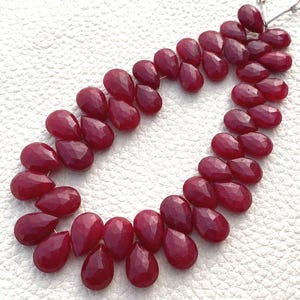 May include: Strand of faceted, teardrop-shaped ruby gemstones. The deep red stones are strung together, showcasing their polished surfaces and unique cuts. Ideal for jewelry making, these gems offer a rich color and sparkle.