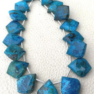 Puede incluir: Un hilo de cuentas facetadas con forma de diamante irregular en tonos vibrantes de azul y turquesa con inclusiones de matriz marrón oscuro. Las cuentas están ensartadas en un hilo plateado, mostrando una superficie pulida y patrones.