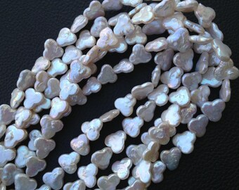 Peut inclure: Gros plan sur des rangées de perles blanches en forme de pétales. Les perles ont un éclat irisé, avec des reflets roses et bleus. Les perles sont enfilées ensemble, créant une forme fluide. Le fond est de couleur sombre et neutre.