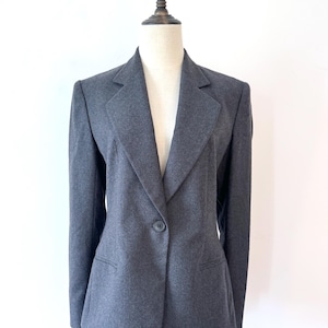 May include: A charcoal gray blazer with a single-button closure and notched lapels. The blazer has two front pockets and is displayed on a mannequin. The jacket is a classic style, suitable for professional or formal wear.