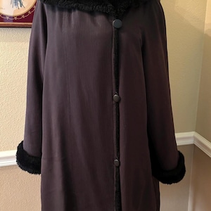 Pode incluir: Um casaco castanho escuro com capuz e acabamento em pele sintética preta. O casaco tem fecho de botões e punhos de pele sintética preta. O casaco é exibido em um manequim.