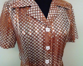 Puede incluir: Un vestido de lunares marrones y blancos con cuello y mangas cortas. El vestido tiene cierre de botones y cintura ajustada.
