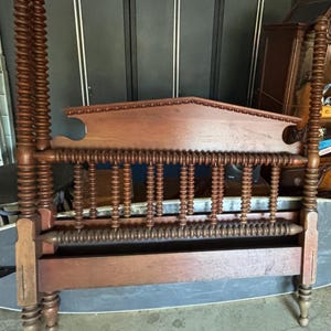 Peut inclure: Un cadre de lit en bois brun foncé avec une tête de lit décorative. Les montants du lit présentent un motif en spirale. La tête de lit a un dessus incurvé et des détails de broche. Le cadre est en bois et semble bien fait.