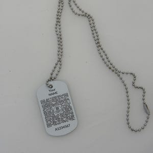 May include: A silver dog tag necklace with a silver chain. The dog tag has a QR code, the text "Your Name", and the number "A1234567".
