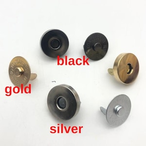 Puede incluir: Varios cierres magnéticos redondos en negro, dorado y plateado. Los cierres tienen un agujero central y un pasador para la fijación. Las palabras "black", "gold" y "silver" están escritas en texto rojo.