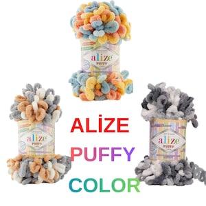 Peut inclure: Trois contenants de fil Alize Puffy Color, aux combinaisons de couleurs variées. La laine a une texture douce et bouclée, avec des couleurs comme le bleu, l'orange, le jaune, le gris et le blanc. Le texte "ALIZE PUFFY COLOR" est affiché en grandes lettres colorées.
