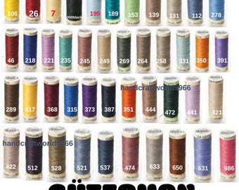 Op de afbeelding: Een verzameling Gütermann-garenspoelen in verschillende kleuren, waaronder geel, rood, zwart, blauw, groen en bruin. Elke spoel is genummerd. Het woord "GÜTERMAN" wordt onderaan weergegeven.