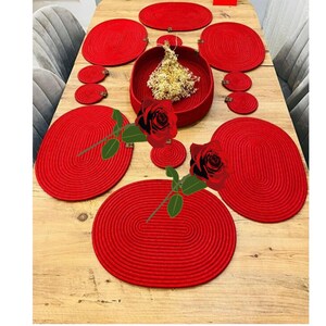 Könnte beinhalten: Ein rotes Esszimmerset mit ovalen Tischsets, runden Untersetzern und einer zentralen Schüssel. Die Artikel sind aus gewebtem Material. Der Tisch hat eine Holzoberfläche.