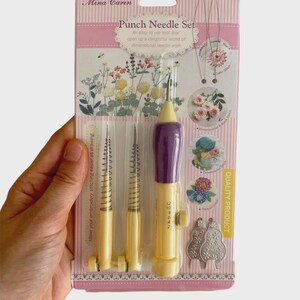 May include: A punch needle set by Mina Carin, packaged on a pink and white card. The set includes a purple and yellow punch needle tool, two additional needles, and a metal template. Text on the package reads "Punch Needle Set".