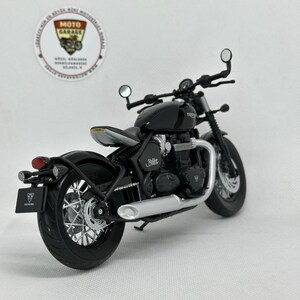 May include: A black motorcycle model with silver detailing, including a round headlight and a curved exhaust. The model has the word "Bobber" on the side and "FOR THE RIDE" on the license plate. The model is a miniature replica.