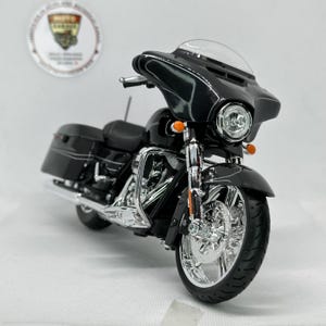 Può includere: Una moto nera con dettagli cromati, parabrezza e borse laterali. La ruota anteriore è in evidenza, mostrando il design dettagliato. La moto ha un aspetto elegante e moderno.