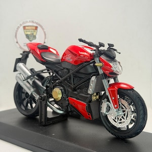 Peut inclure: Une maquette de moto rouge et noire avec le mot "GIANT" sur le côté. La moto a des pots d'échappement argentés, des pneus noirs et un support noir. Le modèle est sur une surface noire.
