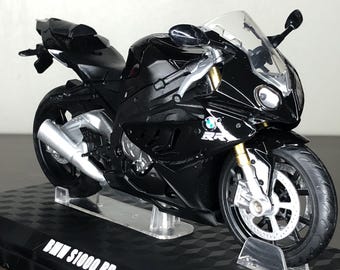May include: A black BMW S1000 RR motorcycle scale model featuring a glossy finish, a clear windscreen, silver exhaust pipes, and detailed wheels. The model is mounted on a black display base with the text BMW S1000 RR printed in white lettering.