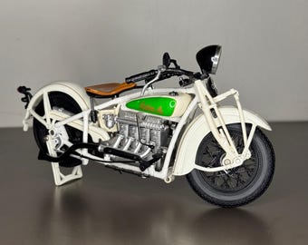May include: White and green vintage motorcycle model with a brown leather seat. The motorcycle has a chrome exhaust and a black headlight.