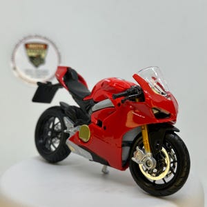 May include: A miniature red and black toy motorcycle with a clear windshield. The motorcycle has black wheels, gold-coloured front forks, and the text "PANIGALE V4" on the side. A detailed replica.