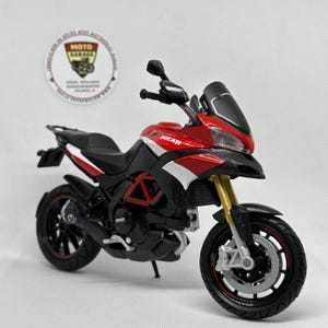 Peut inclure: Modèle réduit de moto Ducati rouge, noire et blanche avec fourches de suspension dorées. Le modèle a une selle, des roues et un carénage noirs. Le mot "Ducati" est visible sur le côté. Réplique détaillée.