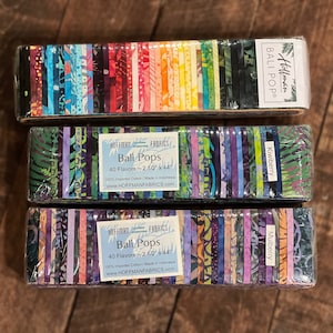 May include: Three packages of Hoffman Bali Pops fabric bundles. Each bundle contains 40 fabric strips, 2.5 inches by 44 inches, in various colors and patterns. The packages are labeled with the names "Kiwiberry" and "Mulberry".
