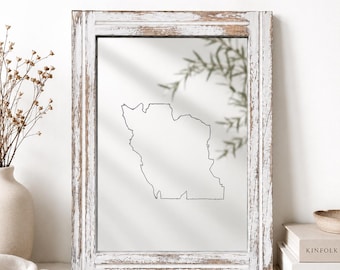 Op de afbeelding: Een rechthoekige wandspiegel met een verweerde wit en bruin houten lijst. Het spiegeloppervlak toont een eenvoudige zwarte lijntekening van een geografische kaartomtrek, waarin een wazige groene plant op de achtergrond wordt weerspiegeld.