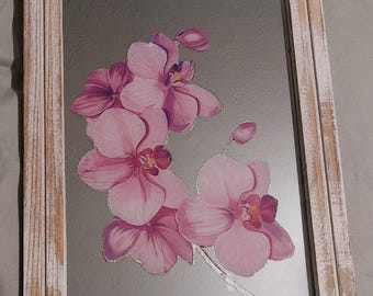Op de afbeelding: Een rechthoekige spiegel met een verweerde witte houten lijst. De spiegel heeft een roze orchidee bloemenontwerp. De orchidee heeft meerdere bloemen en knoppen met een zilveren stengel. De lijst heeft een rustieke, verweerde uitstraling.