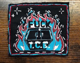 May include: Black square patch with red and blue stitching. The patch features the word "FUCK" above a blue and white image, with the letters "T.C.E." below. Flames and white stars surround the image.