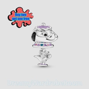 Puede incluir: Un charm plateado con un diseño de tetera y taza, con detalles morados y azules. El charm tiene una apariencia de dibujos animados. La imagen también incluye el texto "Buy two get one free".