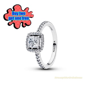 May include: A silver Pandora ring with a square, clear gemstone center, surrounded by smaller stones. The band is also adorned with small stones. The text "PANDORA" is visible on the band. A red and black graphic says "Buy two get one free".