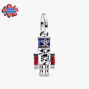 May include: A silver charm in the shape of a toy soldier nutcracker. The nutcracker has a blue and silver hat with a star, red arms, and a white body. The charm has a loop at the top for attaching to a bracelet or necklace.