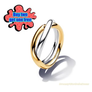 Könnte beinhalten: Ein zweifarbiger Ring mit einem goldenen Band und einem silbernen Band, das sich kreuzt. Der Ring trägt die Aufschrift "PANDORA" auf der Seite. Das Bild enthält auch den Text "Buy two get one free".