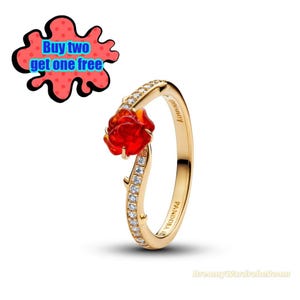May include: A gold ring with a red rose design and sparkling details. The ring has a curved shape, with a red rose at the top and a band set with small, clear stones. The text "Buy two get one free" is in the upper left corner.