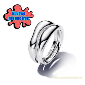 May include: A pair of silver rings with a smooth, curved design. The rings are stamped with the brand name "PANDORA". A red and black graphic with the text "Buy two get one free" is in the upper left corner.